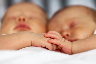 Close-up of two identical twin babies sleeping while cuddling and holding hands